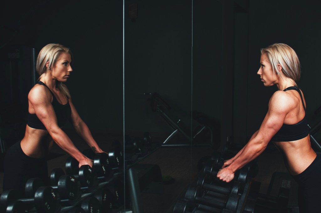 long-haired person in gym looking in mirror.