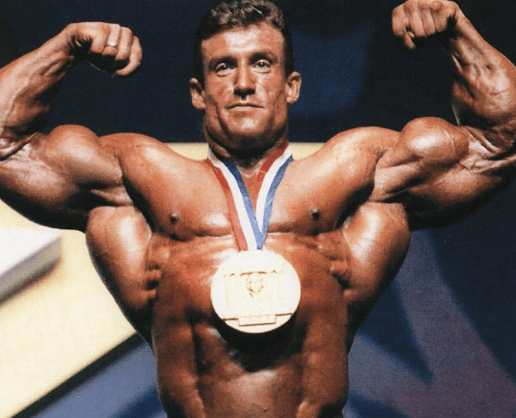 Bodybuilder Dorian Yates flexing muscle while wearing victory medal around neck.